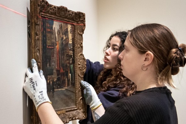 Preparation intern (left) works with museum staff to hang a framed painting